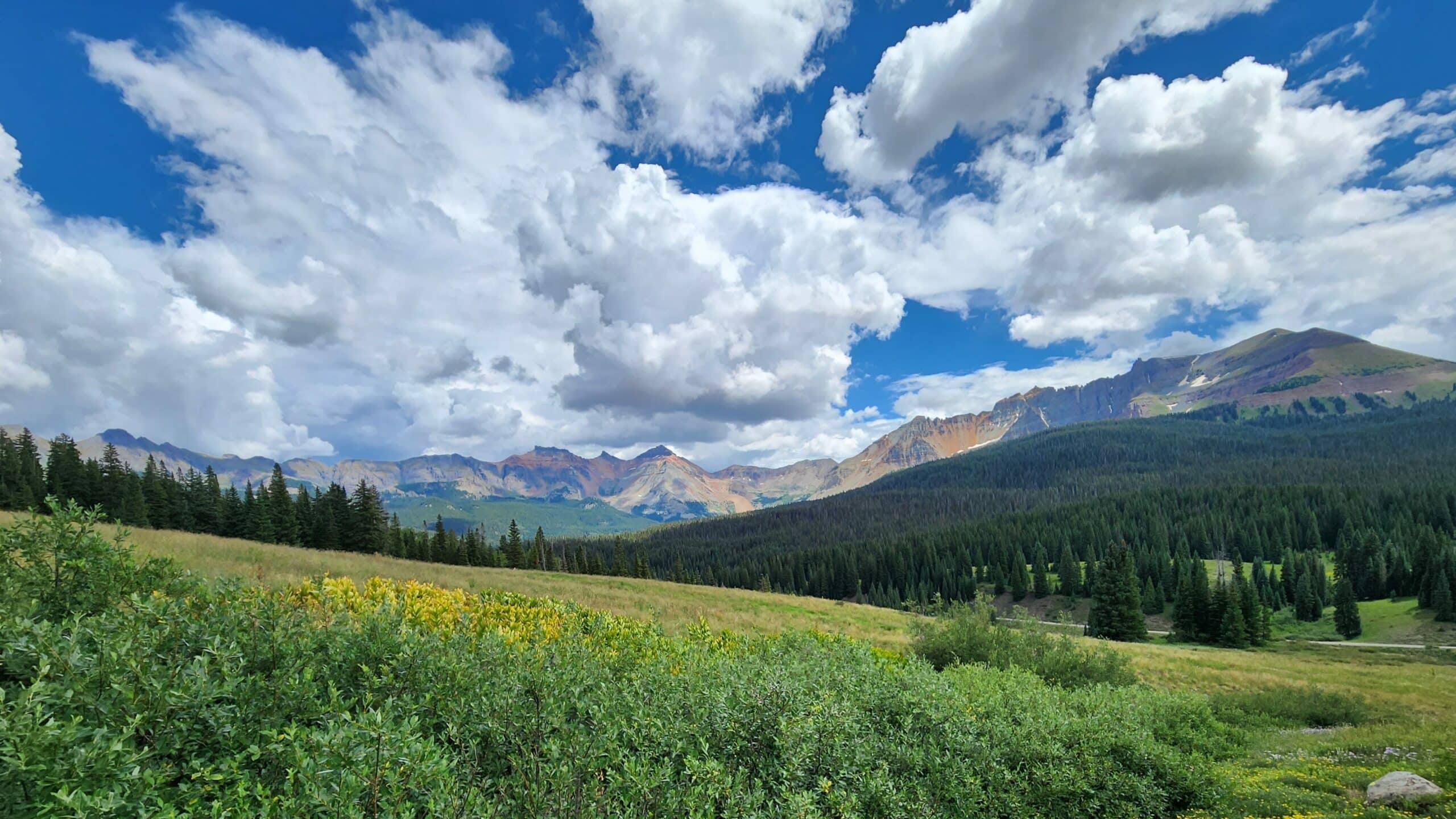 Landscape photo of blue sky with scattered clouds, beautiful green foreground and mountainous midground